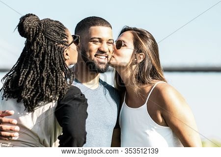 Two Female Friends Kissing African American Man On Meadow. Three Friends Spending Time Together In P