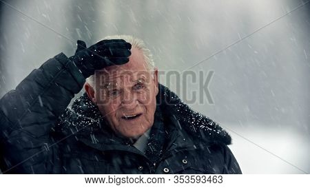 An Old Gray-haired Man Covers His Head Under The Snowfall
