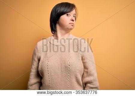 Young down syndrome woman wearing casual sweater over yellow background smiling looking to the side and staring away thinking.