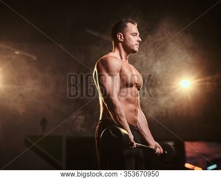 Fit Mucular Bodybuilder Doing Weightlifts With Barbell In A Dark Gym Surrounded By Smoke