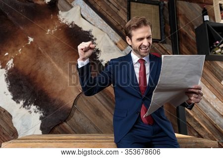 enthusiastic young businessman reading newspaper, holding fist in the air and celebrating victory, sitting in a coffeshop