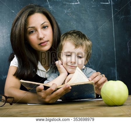 Little Cute Boy In Glasses With Young Real Teacher, Classroom Studying At Blackboard School Kido