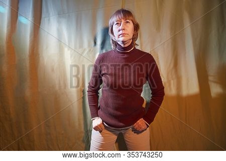 A Middle-aged Woman Poses Showing Clothes Against A Background Of Green Crumpled Curtains. An Inept 
