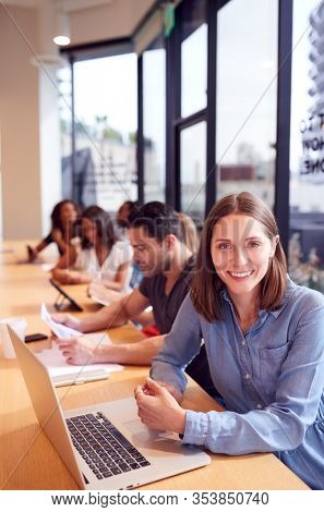 Portrait Of Businesswoman Working At Desk In Shared Open Plan Office Workspace