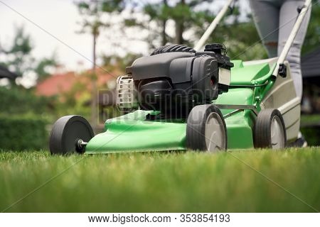 Close Up Of Female Legs In Jeans Of Woman Using Lawn Mower On Backyard. Selective Focus Of Young Gar