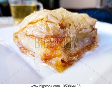 Delicious Greek sweet pastry named Galaktoboureko, made of semolina custard in filo, served with honey in white plate.