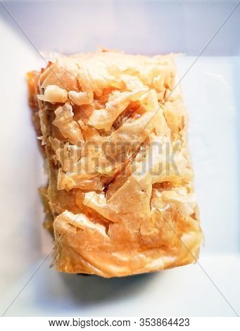 Delicious Greek sweet pastry named Galaktoboureko, made of semolina custard in filo, served with honey in white plate.