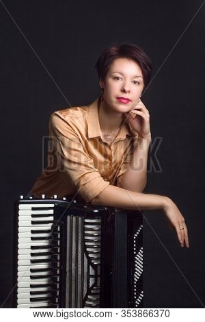 A Brunette In A Gold Shirt, With Short Haircut, On A Dark Kground Of The Studio. With Accordion Musi