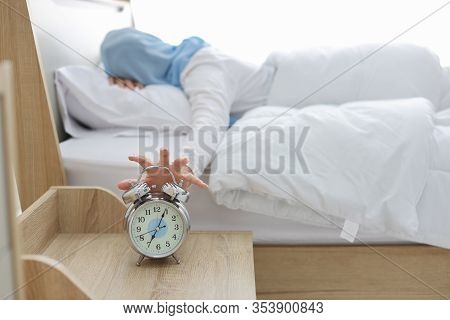 Oversleeping Asian Muslim Woman Wearing White Sleepwear Lying On Bed, Missing Ring Of Alarm Clock Wa
