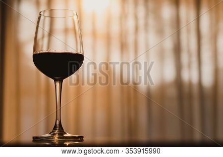 A Glass Of Red Wine On Table In The Room With Sunset Light On Curtian Background.
