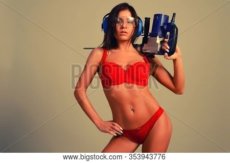 Attractive, Daring Young Woman In Red Lingerie Holds On Her Shoulder A Punch Drill Isolated On Gray 