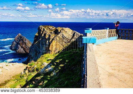 Woman With Camera Take Travel Photo From Seascape Of Atlantic Ocean And Asturias Rocky Coast At Cape