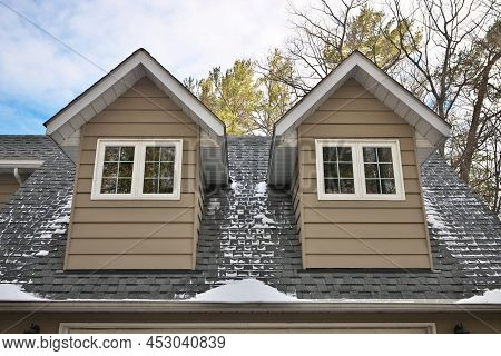Low Angle View Of Dormers Above A Garage In A Home With Beige Gray Wood Siding