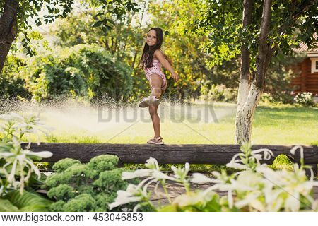 Young Cheerful Girl Walking On Log Smiling Balancing Looking At Camera With Water Sprinklers, Greena