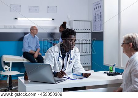 African American General Practitioner Talking To Senior Woman About Health Complications While In He