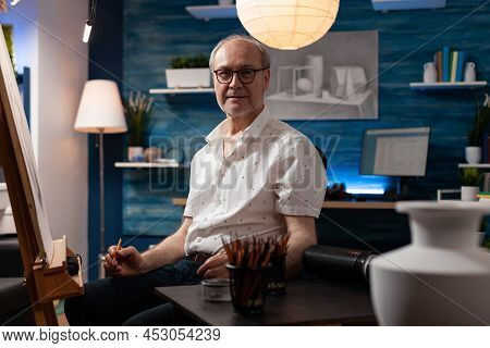 Portrait Of Inspired Elderly Man Posing Confident Holding Pencil In Professional Art Studio Sitting 