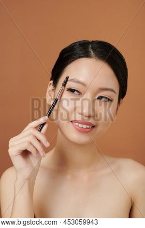Studio Portrait Of Smiling Vietnamese Young Woman Brushing Her Eyebrows