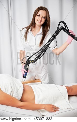 Woman Beautician Looking At Camera And Smiling While Performing Laser Treatment On Female Abdomen. C