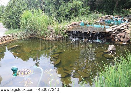 Beautiful Fountain With Rocks And Waterfalls. Fountain In The Park Near Big Green Trees