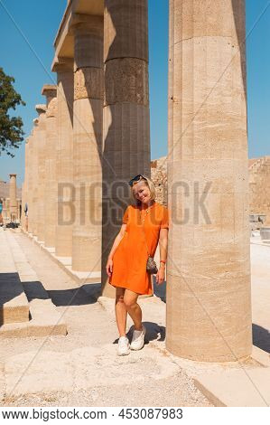 A Woman Stands In The Ancient Acropolis Of Lindos Against The Background Of The Colonade, Greece, Rh