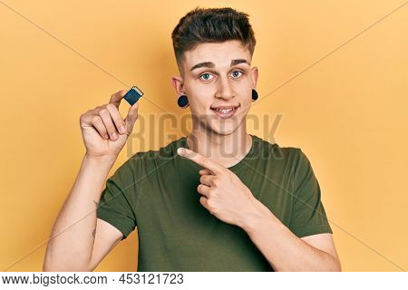 Young caucasian boy with ears dilation holding sdxc card smiling happy pointing with hand and finger 