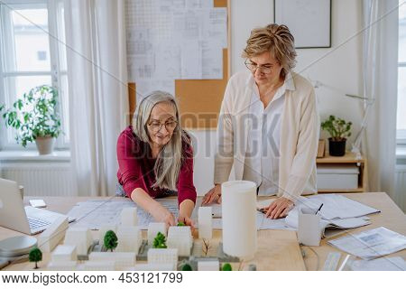 Mature Women Eco Architects With Model Of Modern Bulidings And Blueprints Working Together In Office