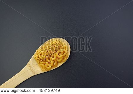 Small And Large Elbow Paste In A Wooden Spoon On A Gray Background.