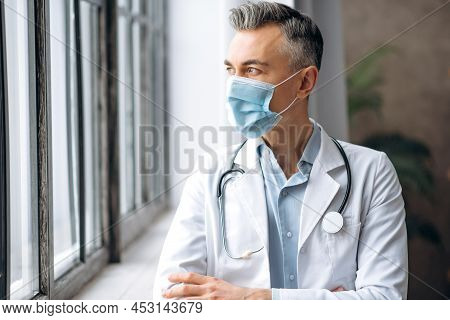 Male Medical Spezialist, Middle-aged Caucasian Doctor, In A Medical Uniform And A Protective Mask, S