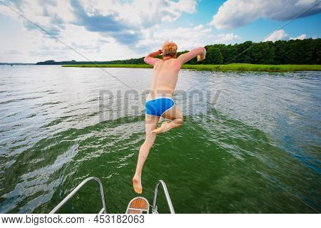 Young Man Jumping From A Sailing Yacht Deck Into A Lake, View From Back