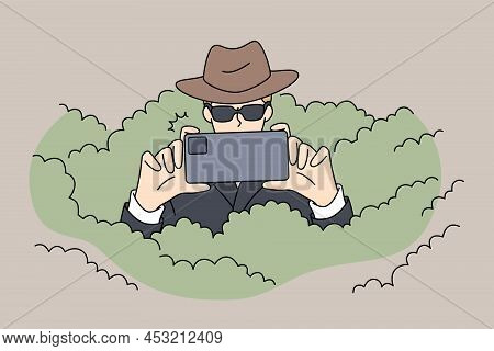 Private Detective In Sunglasses Hiding In Bushes Photographing Using Smartphone Camera. Spy Or Secre