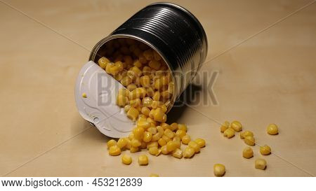 Yellow Corn Is Scattered On The Table. A Can Of Canned Corn With Juice Is Open And Stands On A Woode