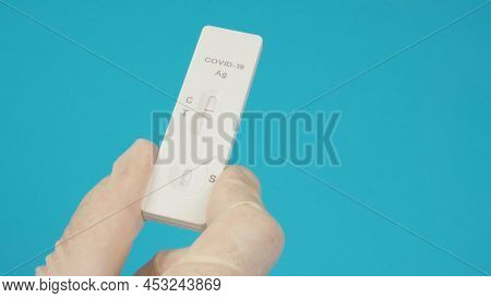 A Hand Hold Atk ( Antigen Test Kit) And Wear Medical Glove On Blue Background.