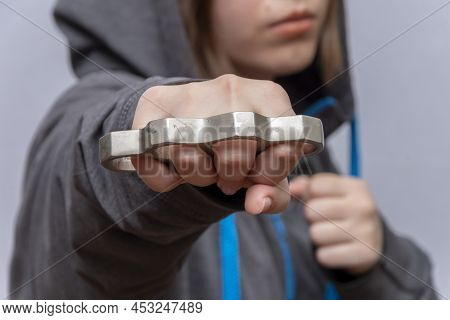 A Teenage Girl Strikes With Brass Knuckles On A Light Background, Wearing A Hoodie With A Hood. Conc