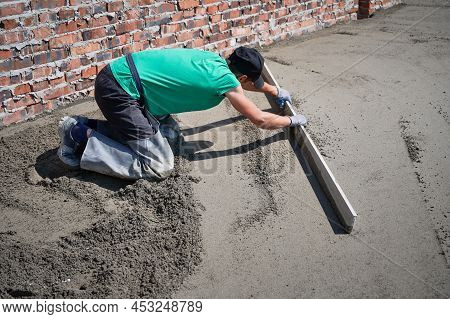 Man Builder Placing Screed Rail On The Floor Covered With Sand-cement Mix At Construction Site On Th