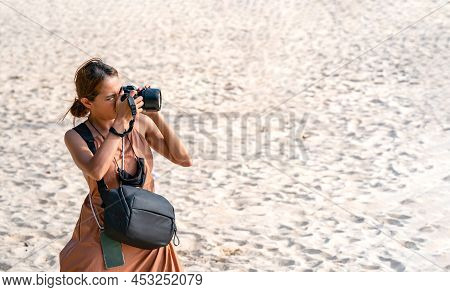 Smart Asian Woman Takes A Photo With Her Digital Camera On The Beach In Afternoon Sunlight.