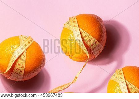 Bright Yellow Measuring Tape Wrapped Around An Orange Isolated On A Pink Background. Close Up