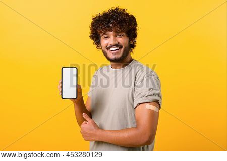 Smiling Curly Indian Man With Medical Band-aid On Arm After The Vaccination Showing Smartphone With 