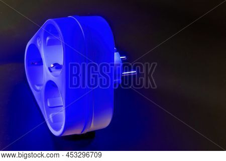 Electrical Three-prong Outlet Adapter With Grounding On A Dark Background