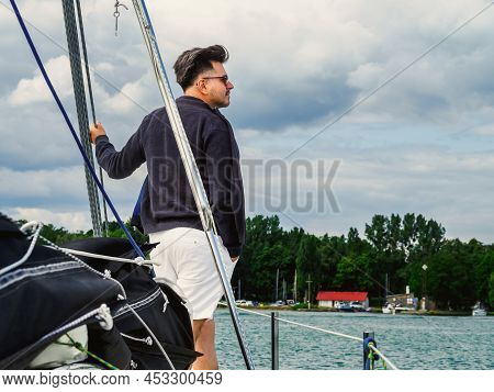 Handsome Person Standing On A Sailing Yacht Bow And Looking A Side In A Cold Day On A Lake, Back Vie