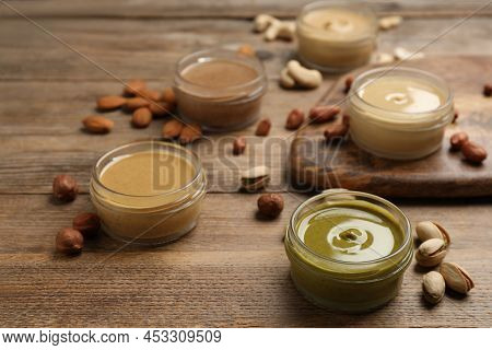 Jars With Butters Made Of Different Nuts And Ingredients On Wooden Table, Closeup