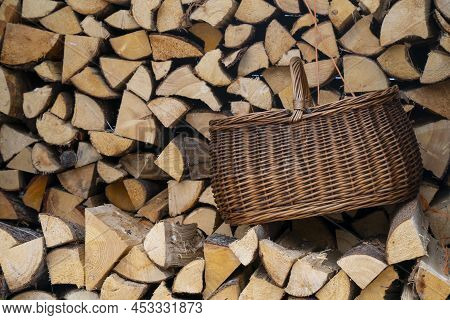 A Wicker Basket Placed On A Large Pile Of Cleaved Firewood.