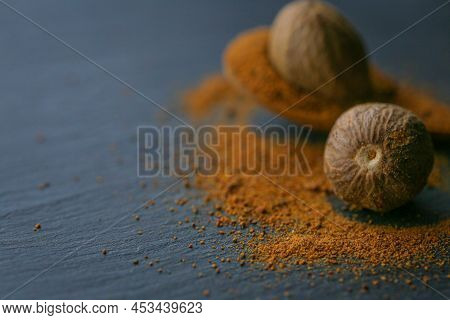 Nutmeg In A Cut And Nutmeg Powder In A Spoon On A Black Background. And Condiments.nutmeg Close-up O