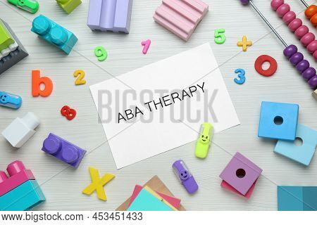 Flat Lay Composition With Phrase Aba Therapy And Colorful Toys On White Wooden Table