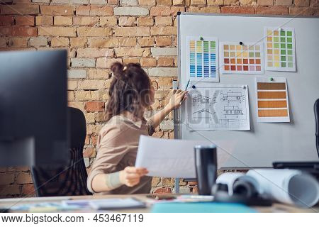 Busy Woman Designer Attaching Blueprint Paper And Color Samples On Board While Working On New Interi