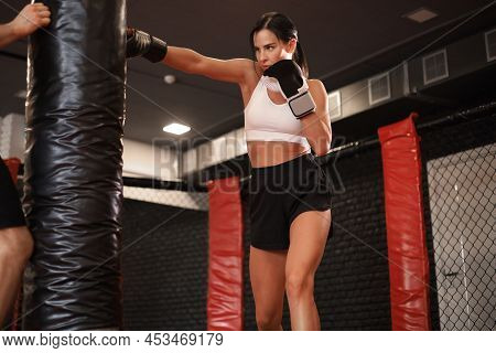 Young Woman Boxer Athletic Wearing Gloves Strikes Punching Bag During Training Preparation For Battl