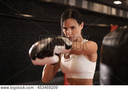 Female In Boxing Gloves And Sportive Wear Stands In A Rack In The Boxing Hall