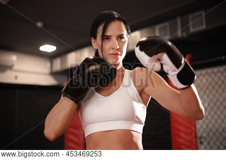 Female In Boxing Gloves And Sportive Wear Stands In A Rack In The Boxing Hall