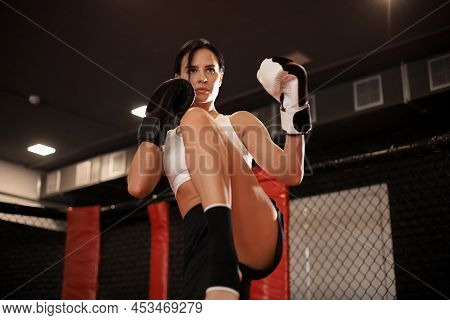 Young Woman Trains In Kickboxing Ring With Heavy Punching Bag. Foot Kicks Or Knee Strike.