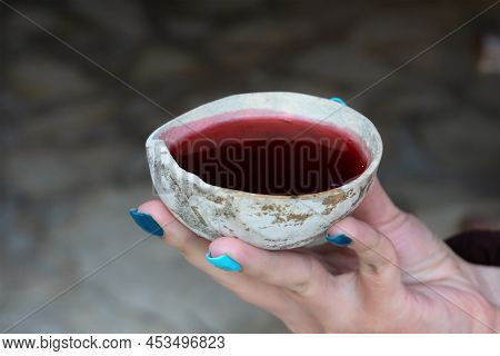 A Woman's Hand Holds A Bowl With A Red Mayan Ritual Drink. Ancient Shell With Hibiscus Tea.