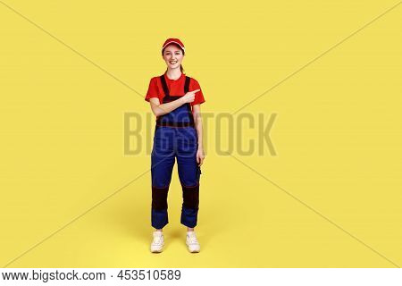 Full Length Portrait Of Optimistic Handy Woman Standing And Pointing Finger Away, Showing Copy Space